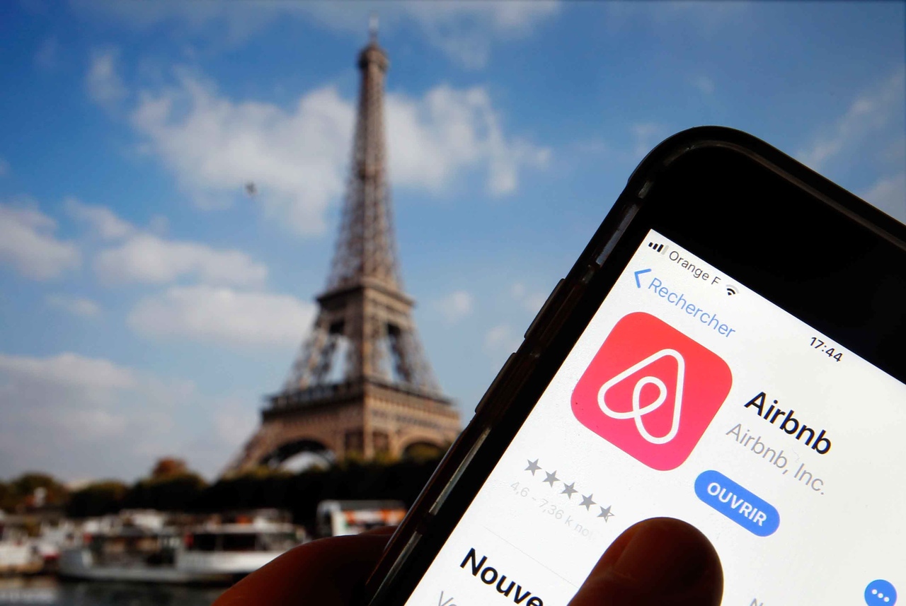 Empresa americana: app do Airbnb aberto na palma da mão. Torre Eiffel no Fundo para simular a França